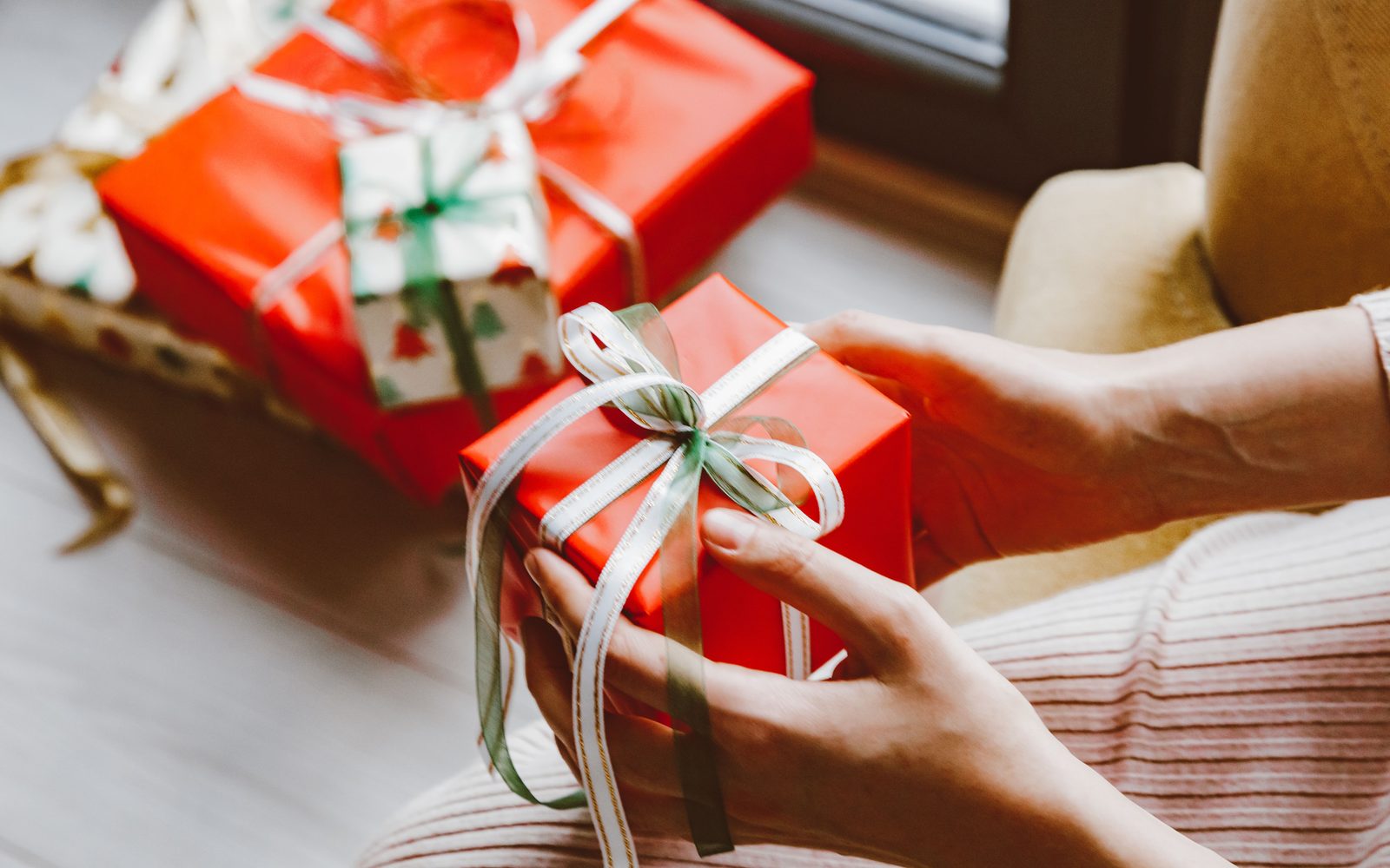 Hands holding a red gift box tied with white and green ribbon